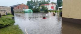Ulewa nad powiatem kościańskim. Na zdjęciu widać zalane podwórko i pomieszczenia gospodarcze, strażacy przy pomocy pompy wypompowują wodę.