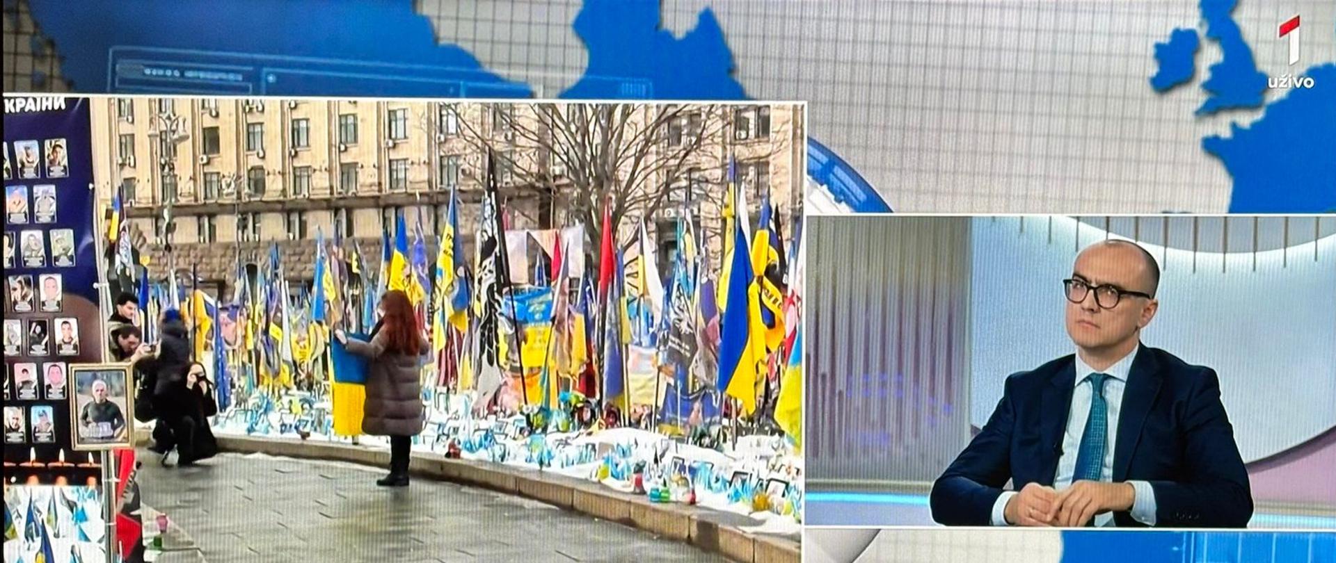 Otpravnik poslova a.i. Bartosz Marcinkowski u emisiji Globus sa desne strane, sa lijeve fotografija ukrajinskih zastava, svijeća i fotografija nastradalih u ratu.