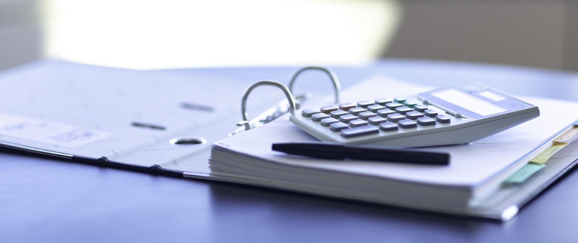 Otwarty segregator z dokumentami, na nim długopis i kalkulator