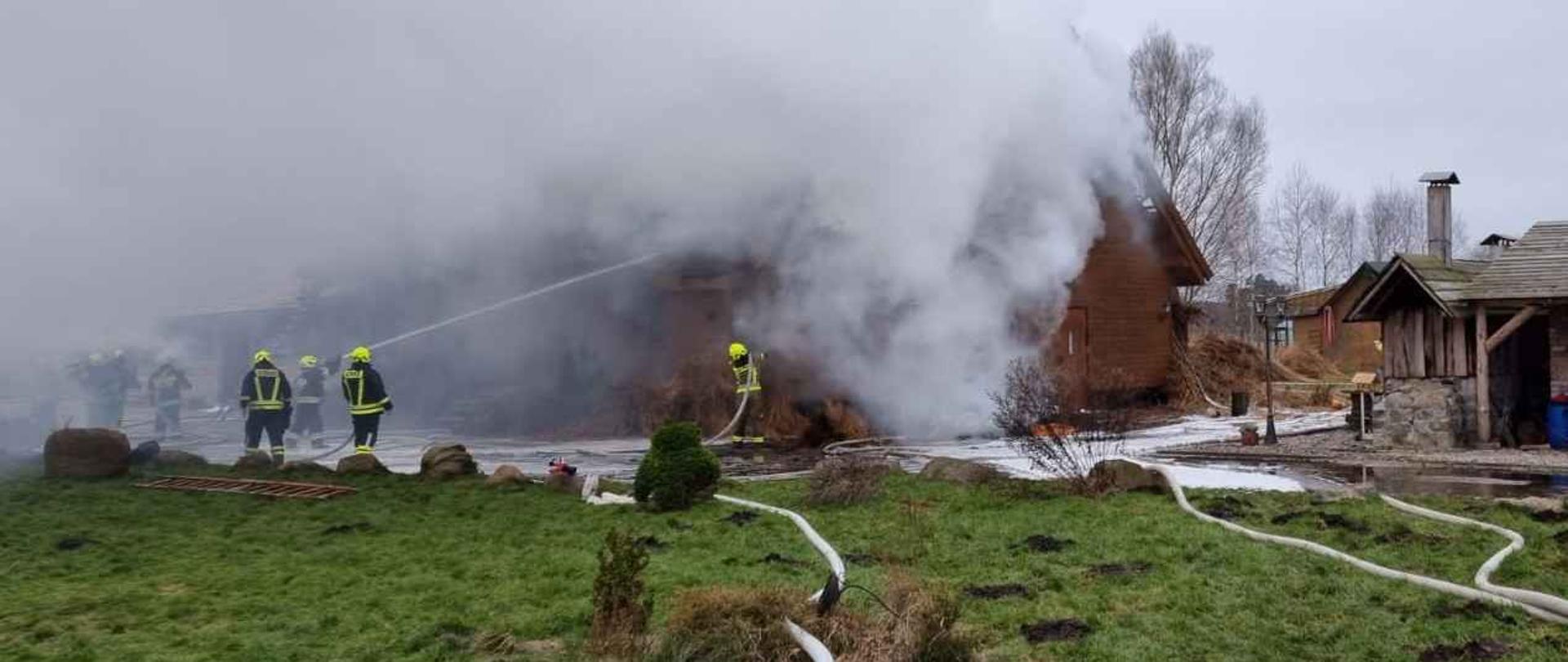 zdjęcie przedstawia budynek objęty pożarem oraz strażaków prowadzących działania gaśnicze