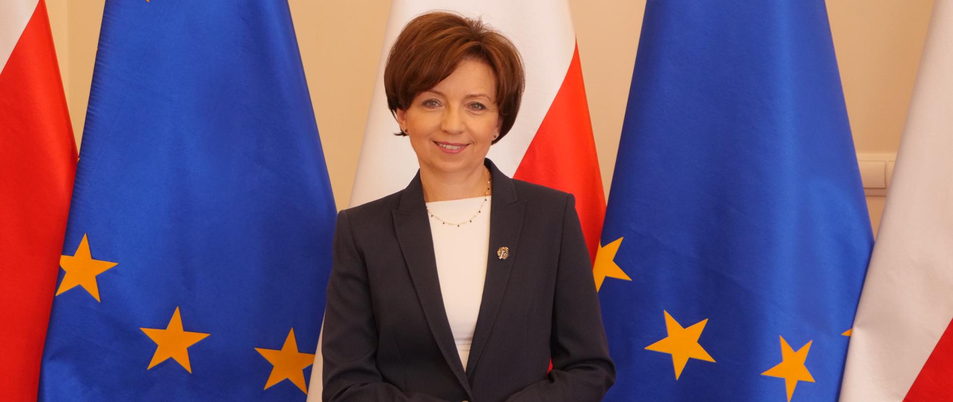 Minister Marlena Maląg na tle flag
