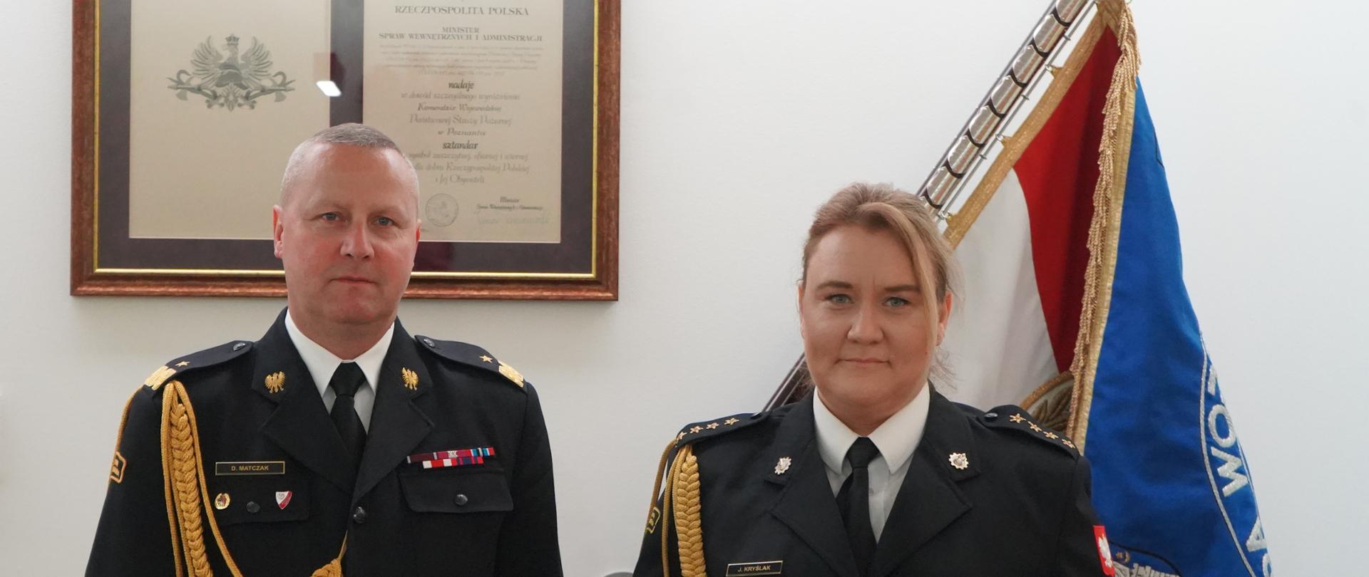 dwóch strażaków, mężczyzna i trzymająca czerwoną teczkę stoi obok siebie , w tle sztandar