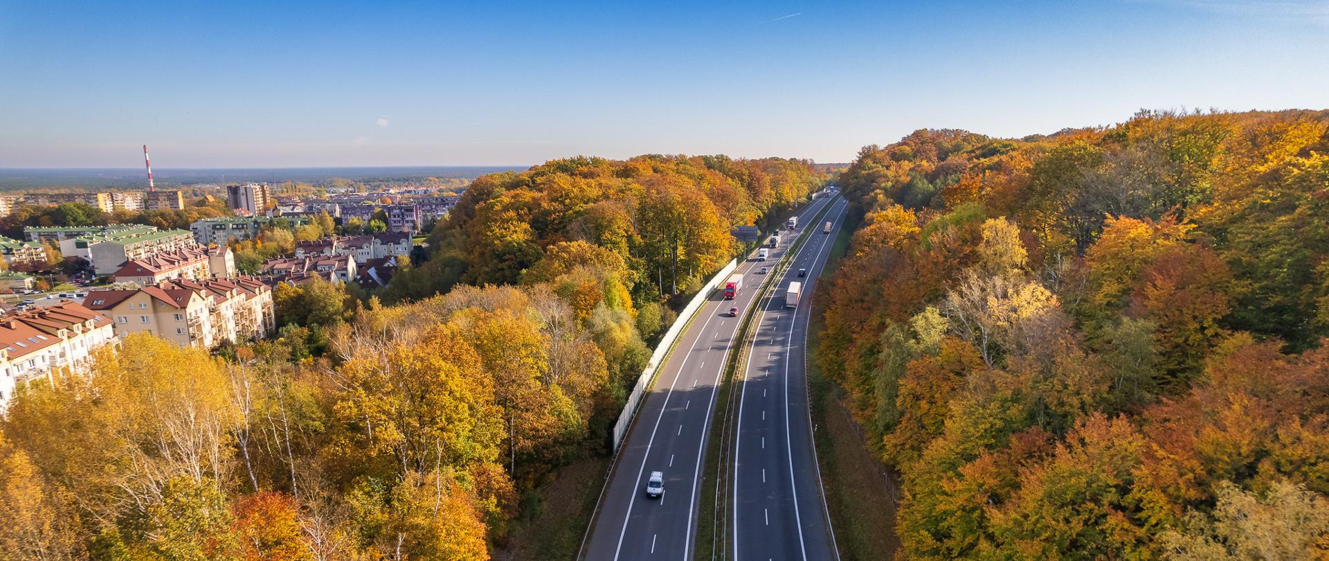 Droga dwujezdniowa przebiegająca przez teren leśny w jesiennej porze z jadącymi samochodami