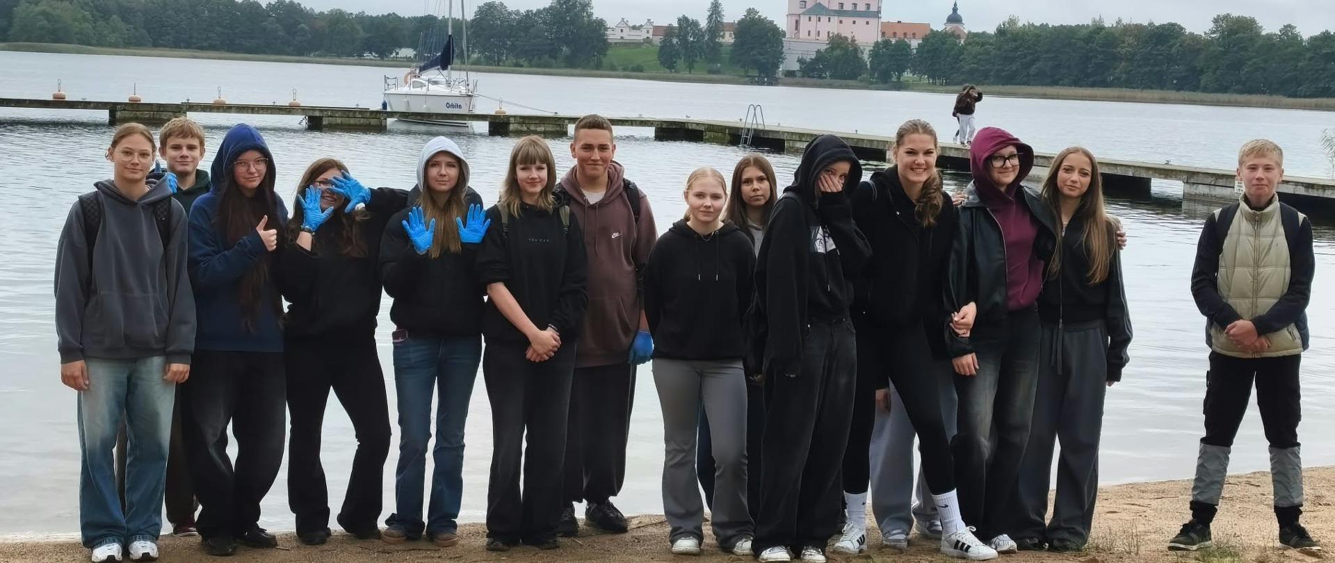 Grupa uczniów na tle jeziora, część osób w niebieskich rękawiczkach.