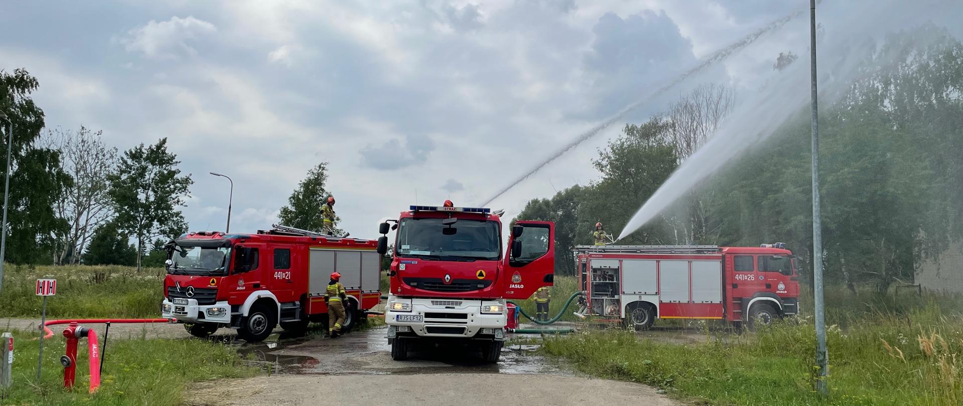 Na zdjęciu trzy samochody gaśnicze i strażacy podają dwa prądy wody