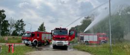 Na zdjęciu trzy samochody gaśnicze i strażacy podają dwa prądy wody. 