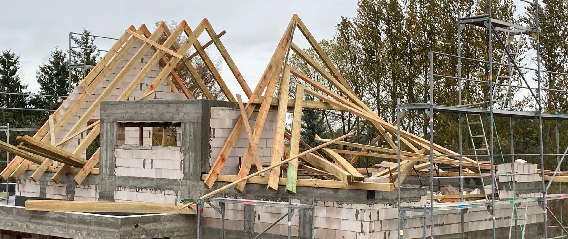Nowobudowany dom jednorodzinny, przy ścianach rozstawione rusztowania, widoczne uszkodzenia ściany i więźby dachowej, 