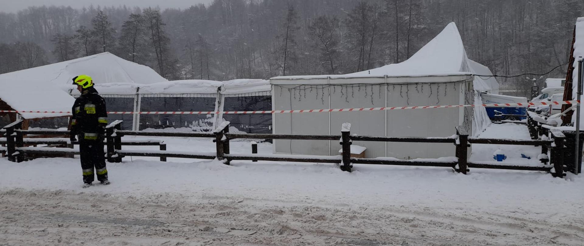 Na pierwszym planie widać strażaka, który zabezpiecza teren akcji, za nim widoczna jest zawalona metalowa konstrukcja namiotu