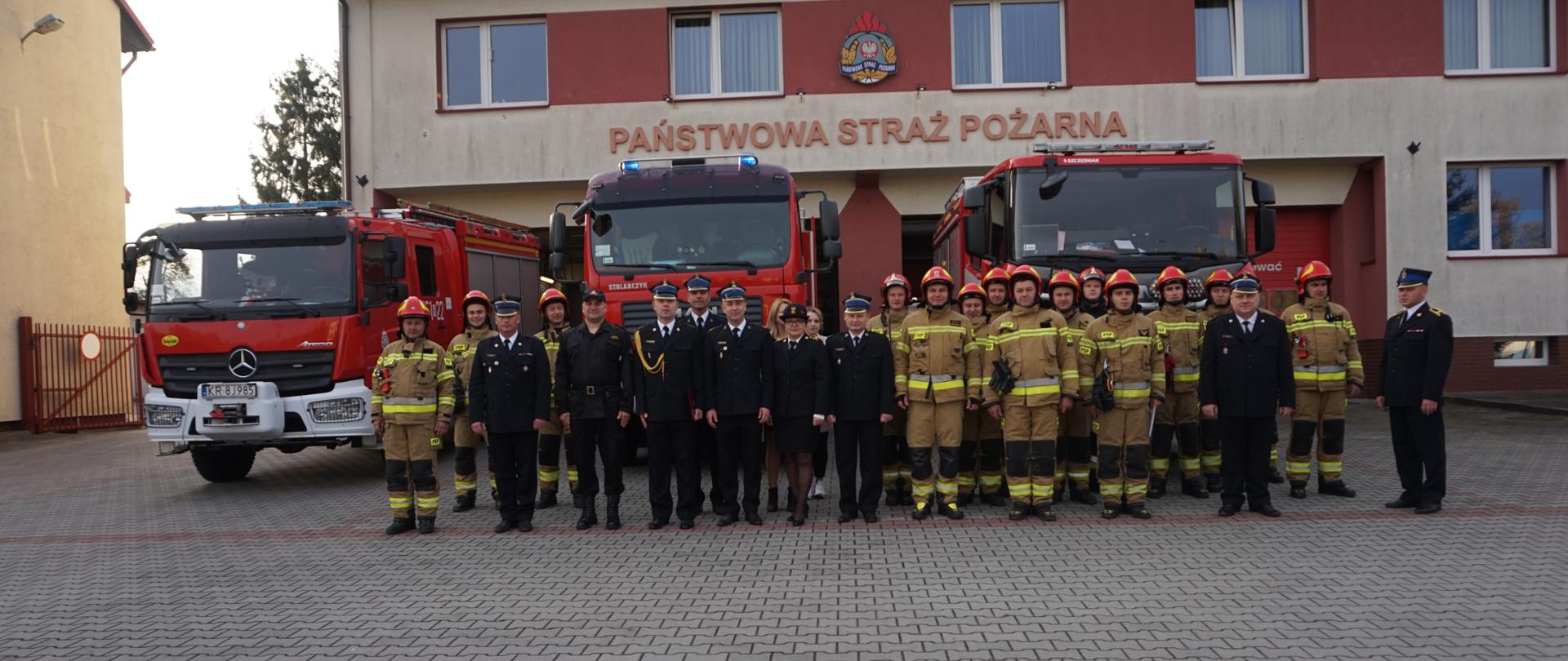 Na zdjęciu widoczni strażacy z Jednostki Ratowniczo- Gaśniczej w Miechowie na tle samochodów pożarniczych oraz budynku jednostki