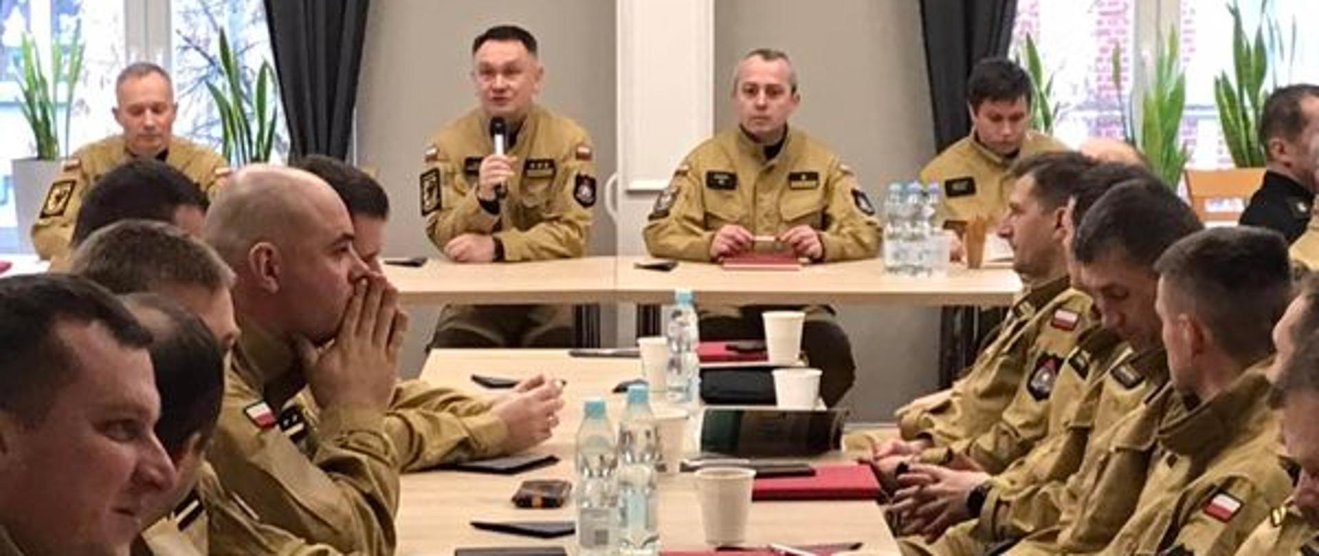 Funkcjonariusze siedzą przy stołach. Odprawę operacyjną dla komend powiatowych i miejskich Państwowej Straży Pożarnej rozpoczyna Zastępca Pomorskiego Komendanta Wojewódzkiego PSP st. bryg. Tomasz Siemiętowski.