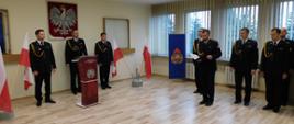 Na zdjęciu widoczni są strażacy w umundurowaniu wyjściowym podczas uroczystej zbiórki z okazji powołania KM PSP w Tarnowie. Jeden z funkcjonariuszy czyta rozkaz o powołaniu Komendanta Miejskiego PSP w Tarnowie.