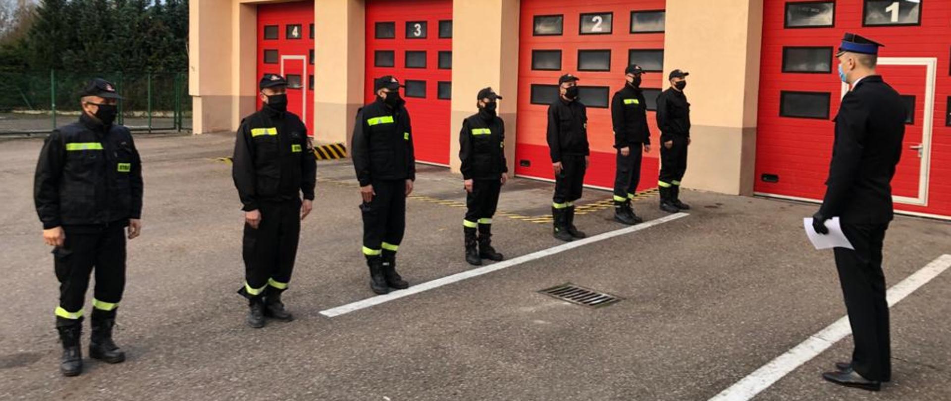 Zastępca Komendanta Powiatowego PSP w Ostródzie st. kpt. Rafał Napiórkowski wręczający akty mianowania na wyższy stopień służbowy w trybie nagrodowym