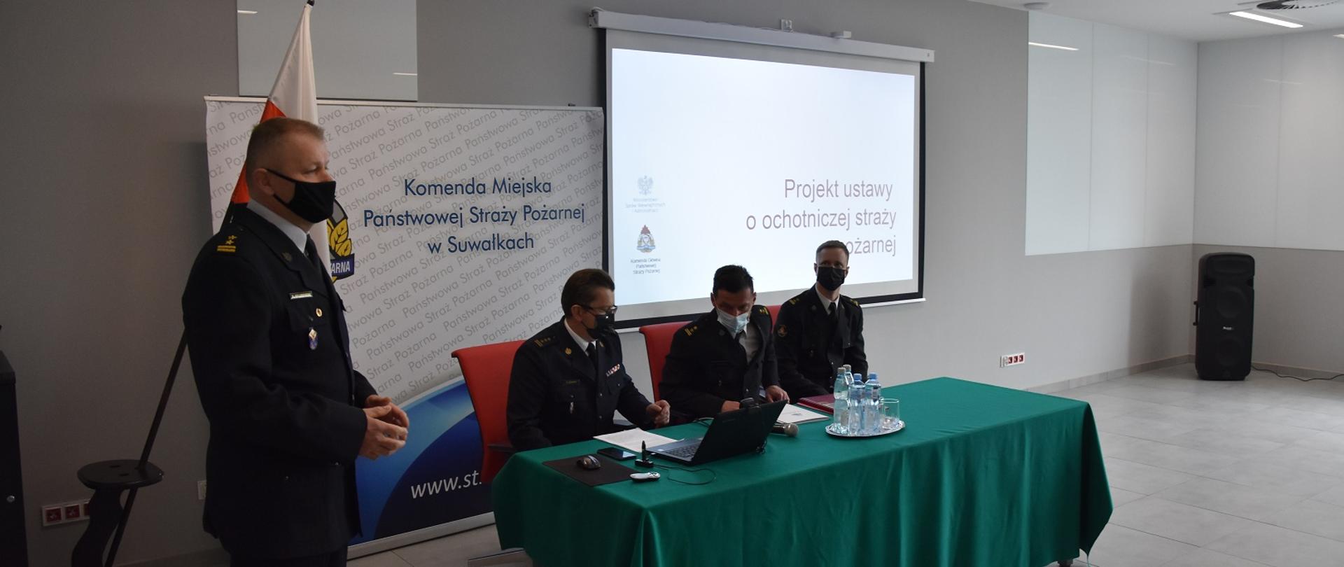 Zdjęcie obrazuje 4 strażaków w mundurach wyjściowych w tle flaga Polski 
