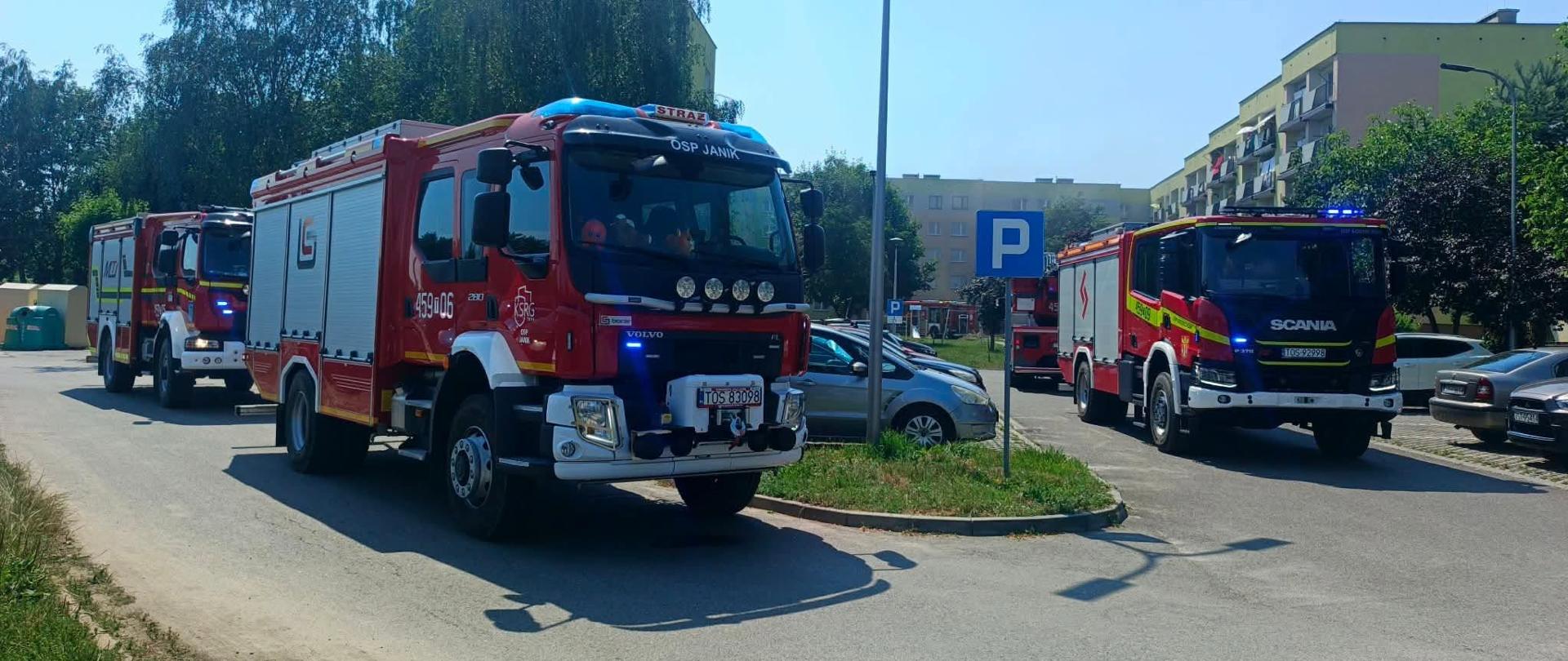 Na zdjęciu widoczne są wozy strażackie na parkingu przed blokiem 