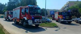 Na zdjęciu widoczne są wozy strażackie na parkingu przed blokiem 