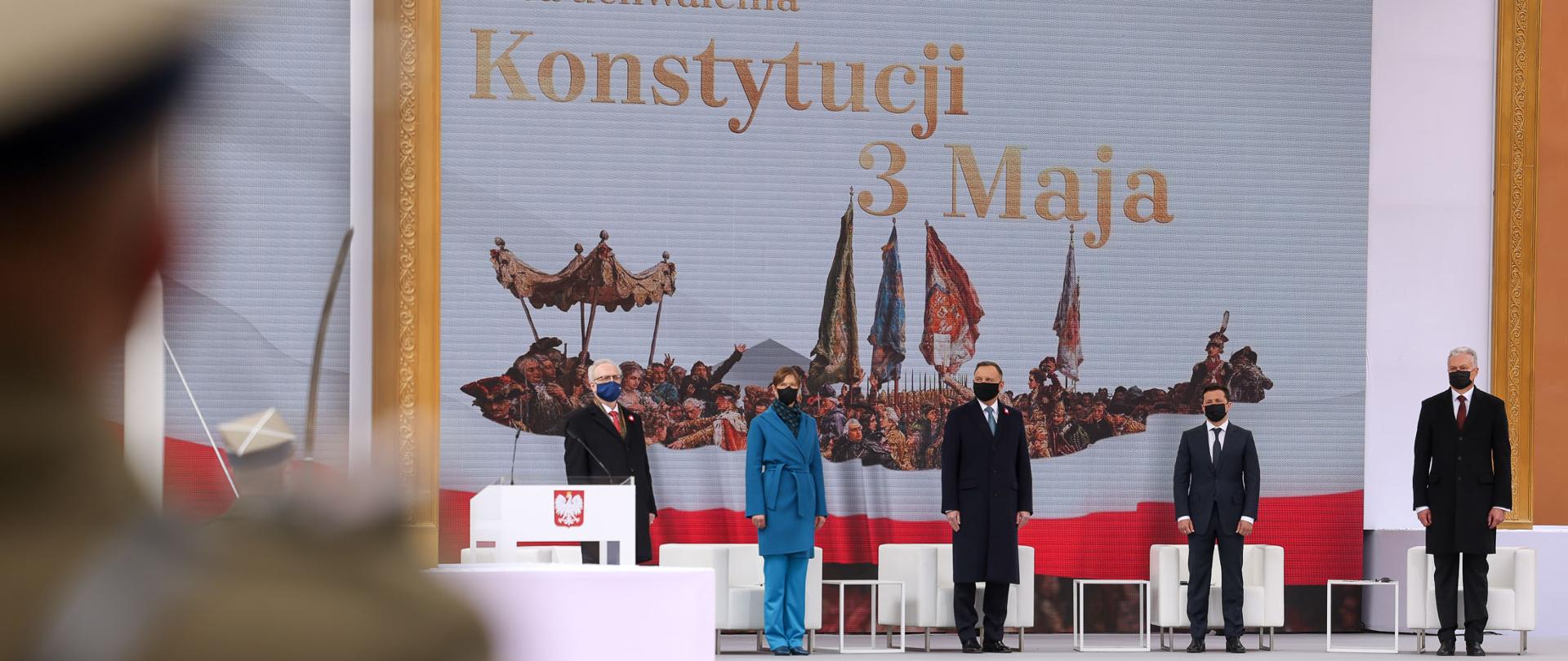 Na zdjęciu prezydenci Polski, Litwy, Łotwy, Estonii i Ukrainy stojący na scenie. W tle telebim przedstawiający fragment obrazu Jana Matejki oraz napis 230. rocznica uchwalenia Konstytucji 3 Maja. 
