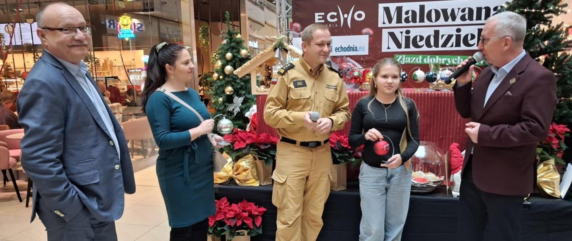 Zdjęcie przedstawia miejsce zastępcę komendanta miejskiego PSP w Kielcach z rodziną podczas przekazywania malowanej własnoręcznie bombki. 