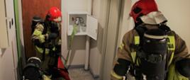 Trzech strażaków ubranych w aparatach ochrony układu oddechowego na klatce schodowej 
