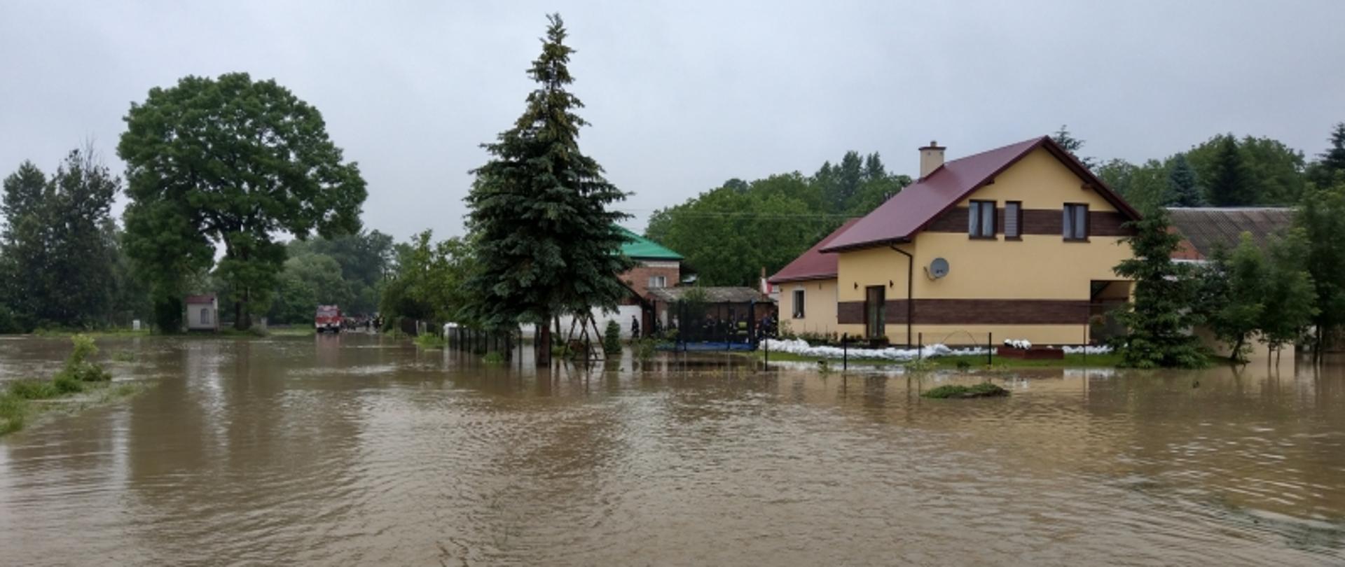 Na zdjęciu widoczny jest wysoki stan wody po wylaniu rzeki, a także dom zabezpieczony workami z piaskiem