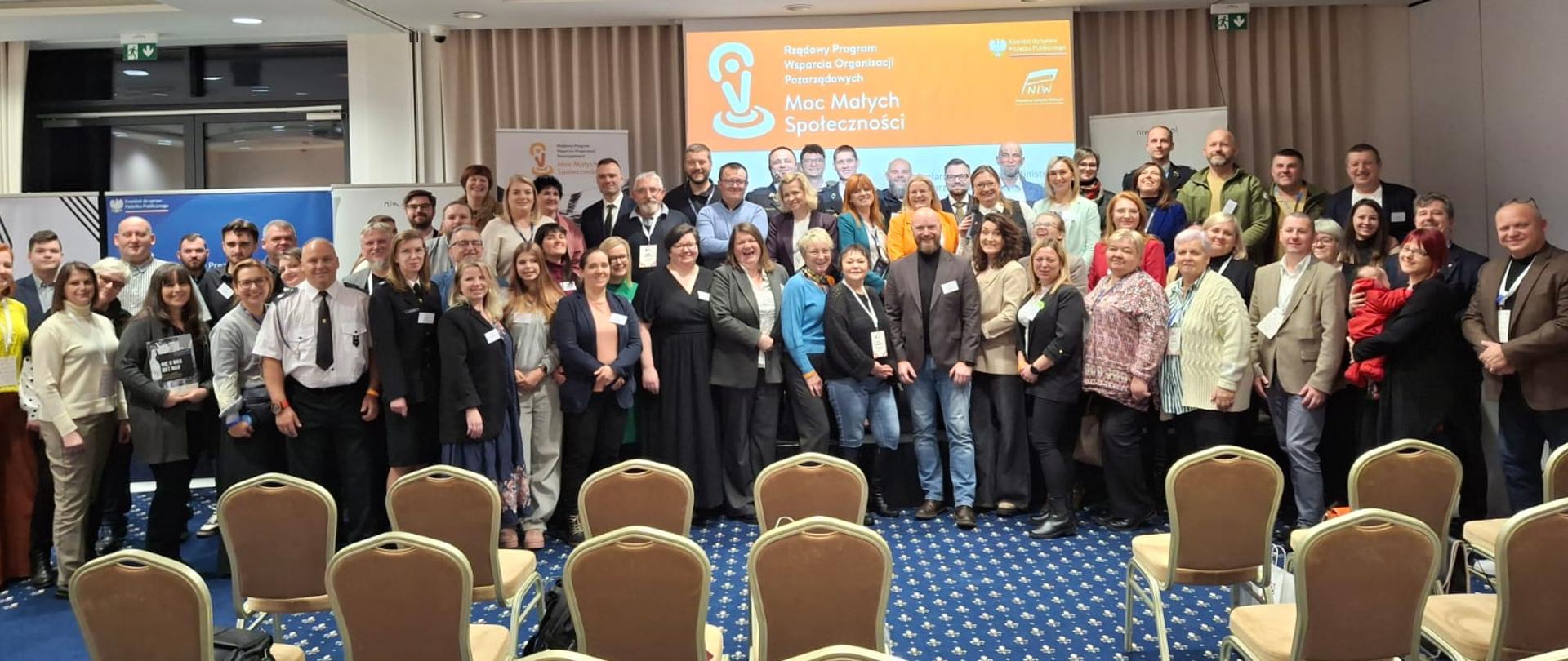 Szeroki kadr, zdjęcie grupowe. Uczestnicy wydarzenia pozują do wspólnego zdjęcia. 