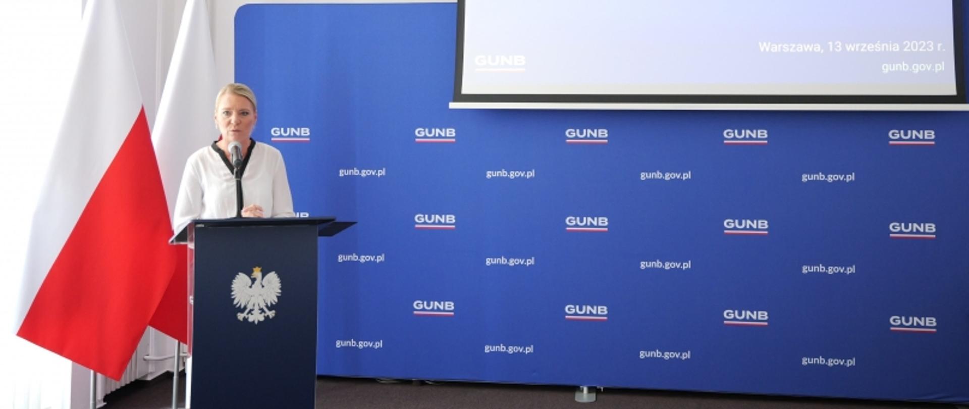 Wystąpienie przy mównicy z flagą Polski i tłem z logotypami GUNB oraz adresem „gunb.gov.pl”; na ekranie data „Warszawa, 13 września 2023 r.”.