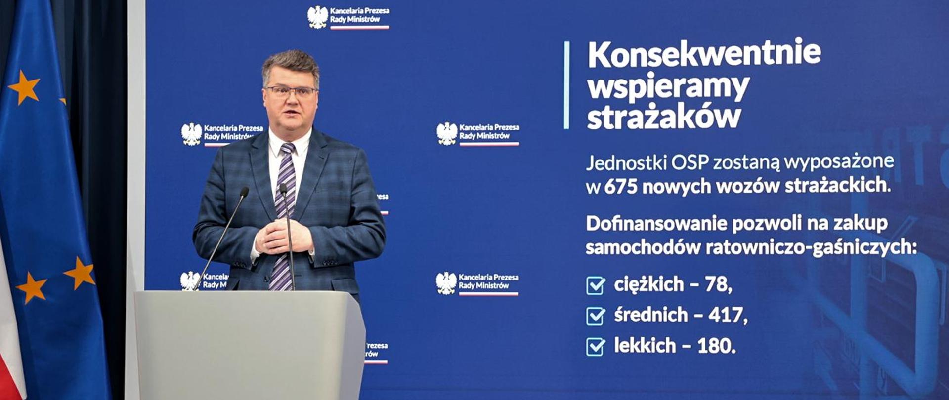 Zdjęcie przedstawia wiceministra Macieja Wąsika podczas konferencji dotyczącej dofinansowania na zakup samochodów ratowniczo-gaśniczych dla Ochotniczych Straży Pożarnych w 2023r