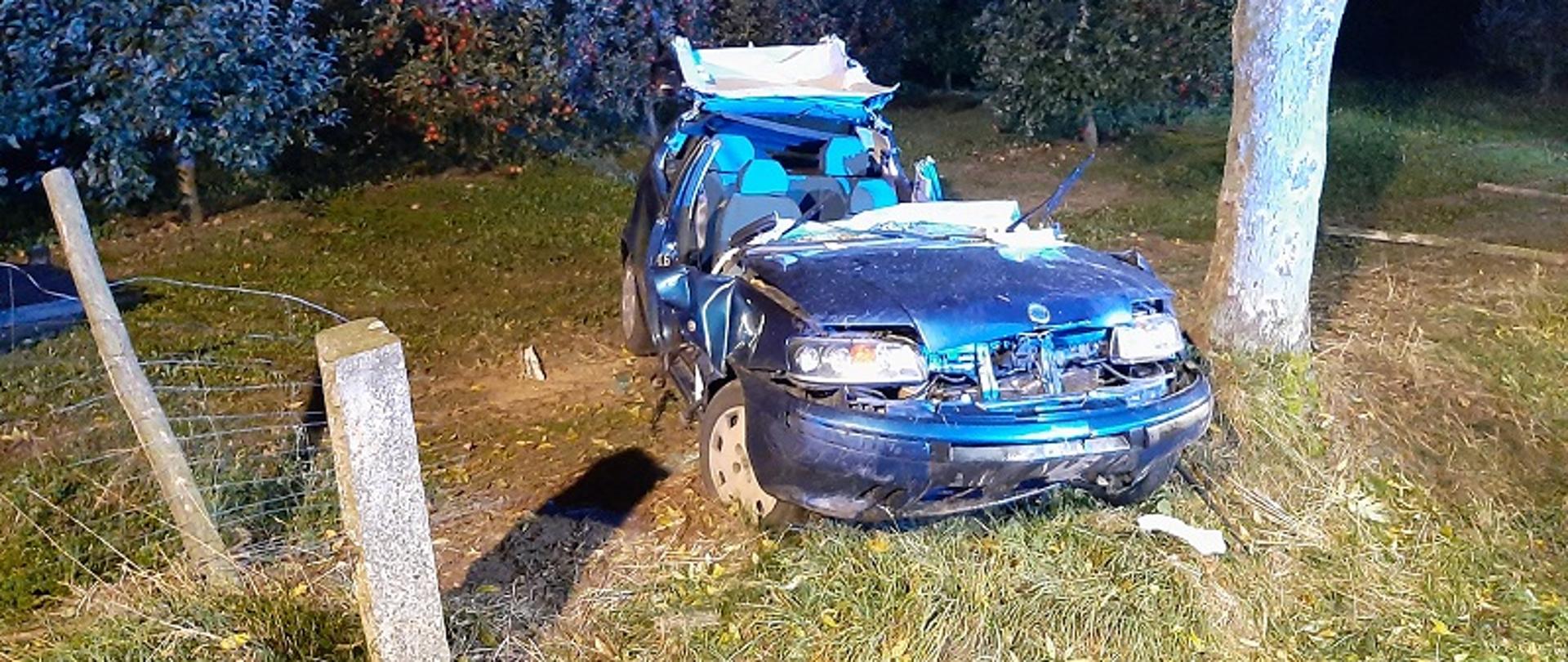 Zdjęcie przedstawia samochód osobowy marki Fiat Punto, który w porze nocnej uderzył w drzewo. Samochód ma całkowicie odcięty dach w wyniku działań ratowniczych strażaków.