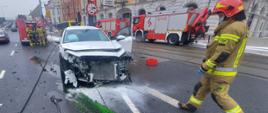 Zdjęcie przedstawia rozbity samochód, trzy samochody pożarnicze oraz strażaków.