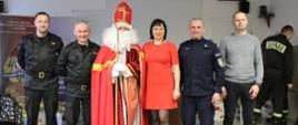 Na zdjęciu widoczny jest Mikołaj wraz z dwoma funkcjonariuszami Państwowej Straży Pożarnej, Komendantem Policji w Krośnie, przewodniczącym związku zawodowego NSZZP przy KMP w Krośnie oraz przewodnicząca IPA Region Krosno.