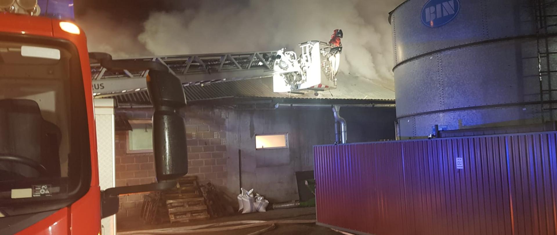 Na zdjęciu widać strażaków działających mechaniczną drabiną na tle budynku, który uległ spaleniu 