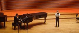 Uczeń grający na puzonie, obok akompaniator przy fortepianie na scenie sali koncertowej PSM