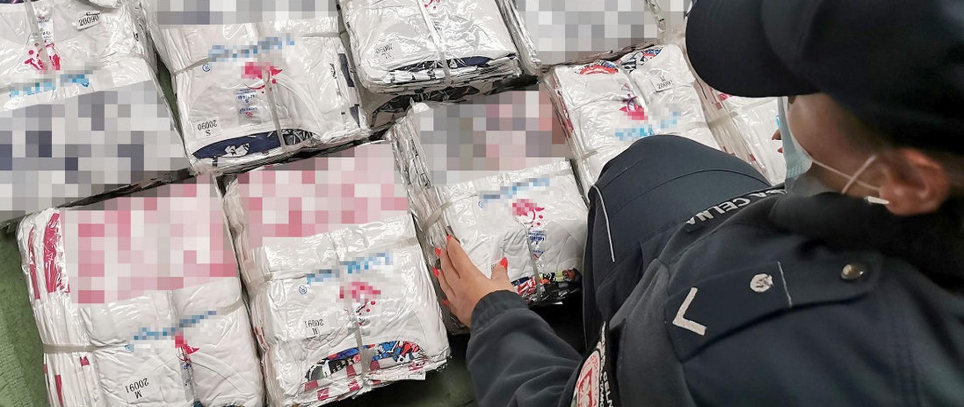 Funkcjonariuszka KAS przy podrobionej odzieży rozłożonej na ziemi.