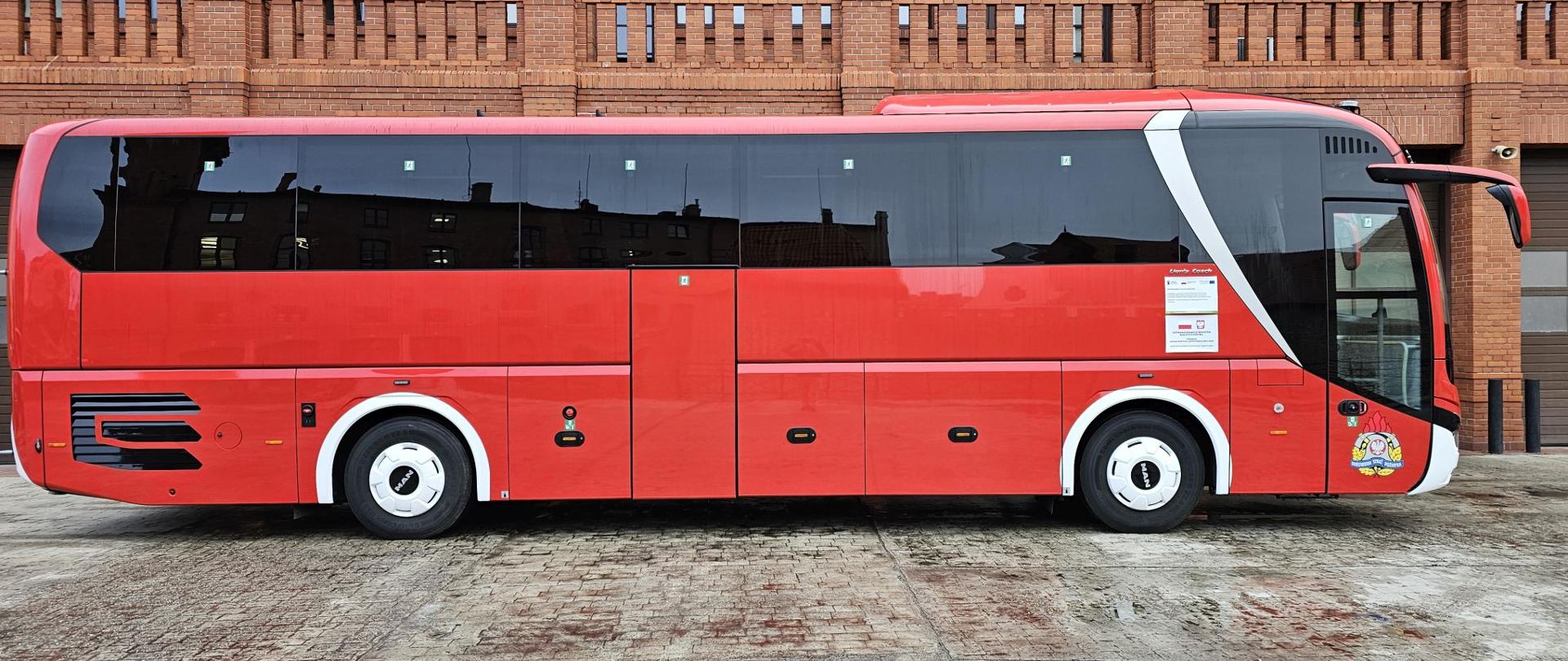 Strażacki autobus w kolorze czerwonym na tle strażnicy