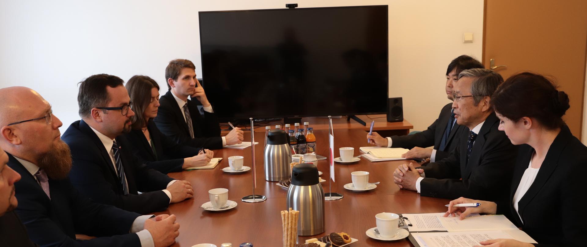 Na zdjęciu widać grupę ludzi, która siedzi przy stole. Po lewej stronie jest 5 osób, po prawej 4 osoby. Ta grupa osób przebywa w sali konferencyjnej.