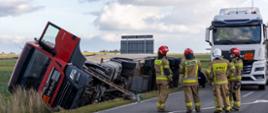 Strażacy zabezpieczają miejsce wypadku z przewróconą ciężarówką w pobliżu turbiny wiatrowej. 
