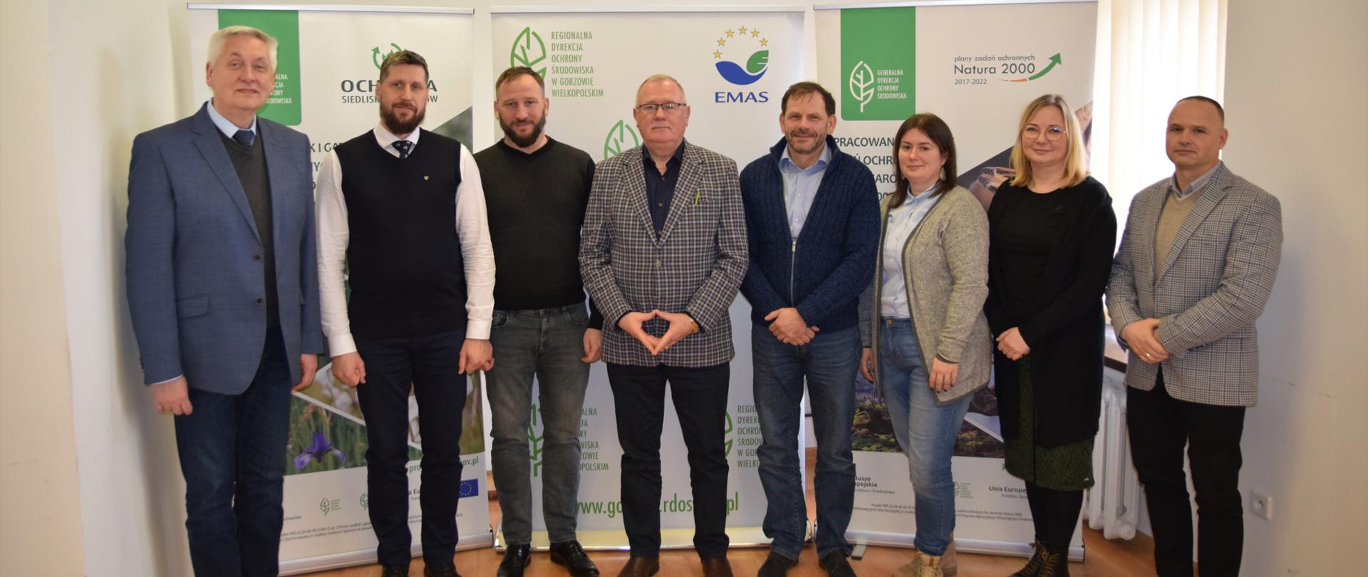 Grupa sześciu mężczyzn i dwóch kobiet pozuje do zdjęcia. Za ich plecami banery z logo w kształcie zielonego liścia i napis Regionalna Dyrekcja Ochrony Środowiska w Gorzowie Wielkopolskim.