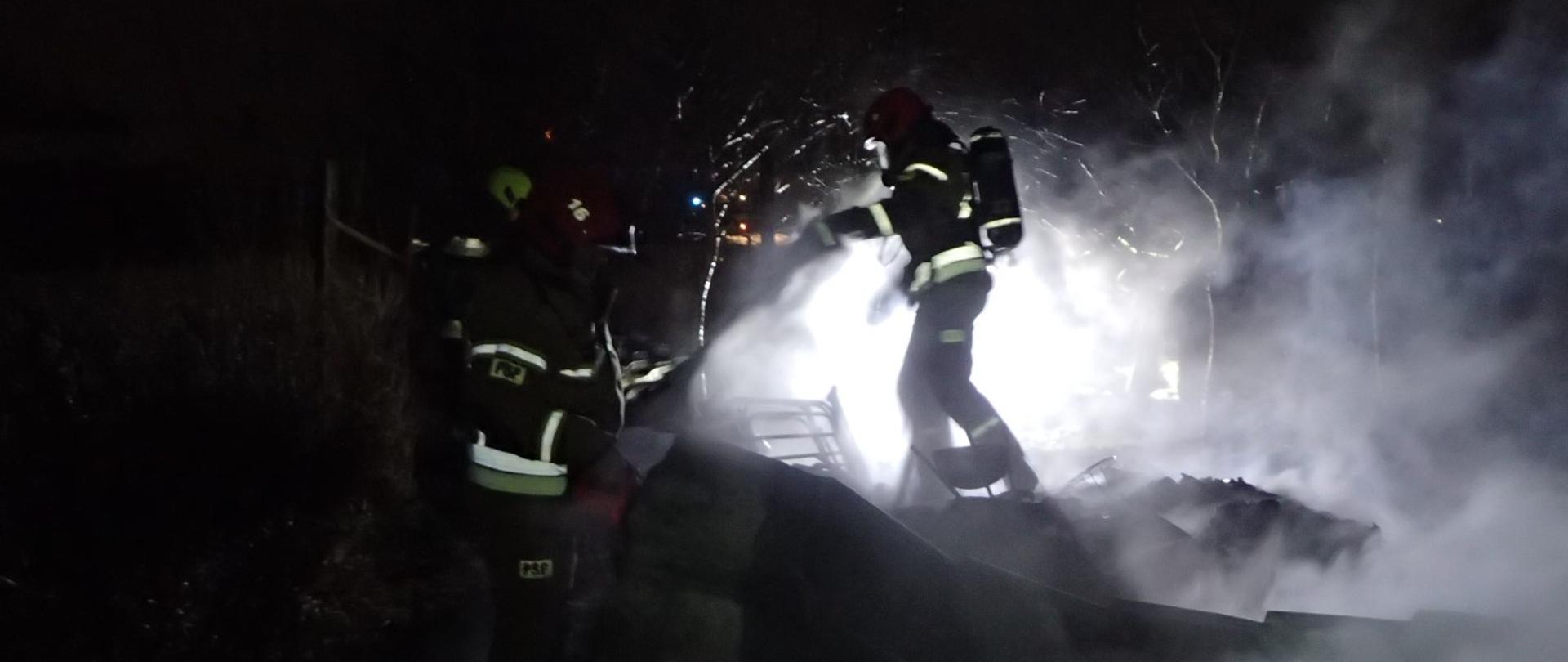 Na zdjęciu strażacy PSP i OSP prowadzą działania gaśnicze w zadymieniu. Dookoła panuje mrok