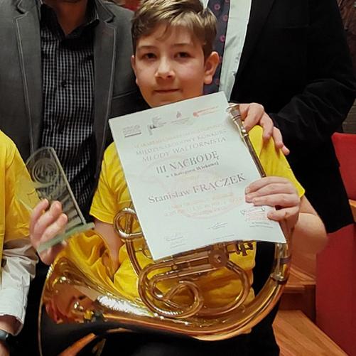 Chłopiec trzyma waltornie, statuetkę i dyplom
