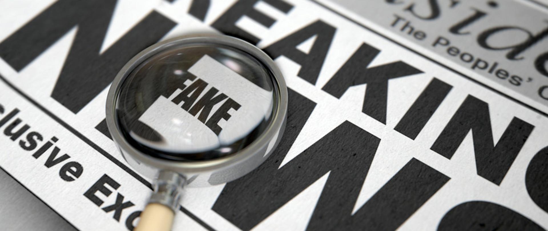 Zdjęcie w poziomie. Gazeta z napisem "Breaking (fake) news". Na niej leży lupa.