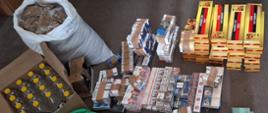 Paczki papierosów i worki z tytoniem i plastikowe butelki ułożone i ustawione na podłodze.