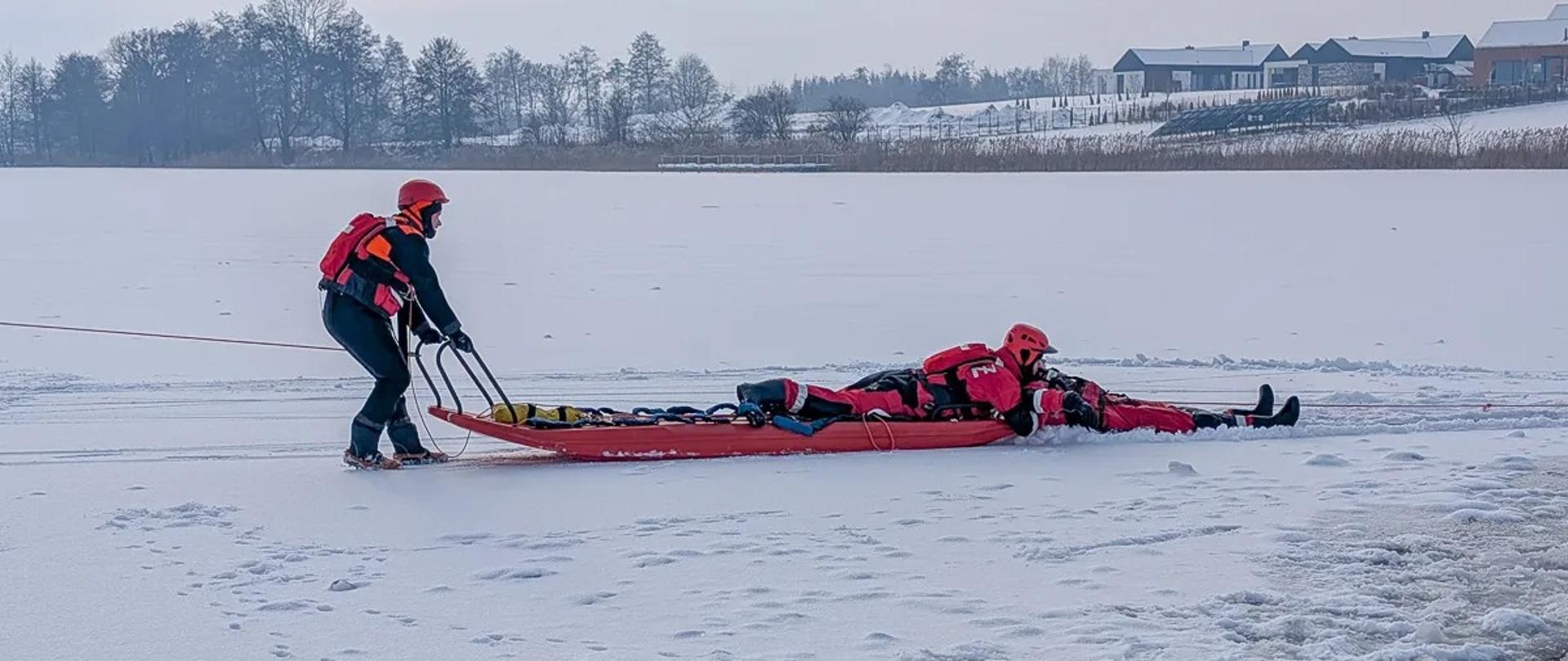 Ratownicy ubrani w ubrania lodowe próbują podjąć innego ratownika z przerębla