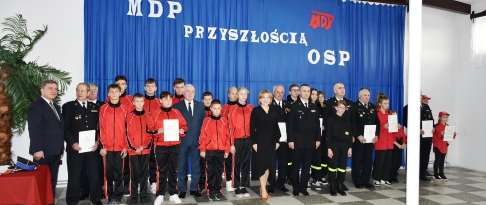 Członkowie MDP oraz prezesi OSP wraz z parlamentarzystami oraz komendantem wojewódzkim i powiatowym pozują do grupowego zdjęcia po wręczeniu promes na zakupy sprzętu umundurowania etc dla MDP.