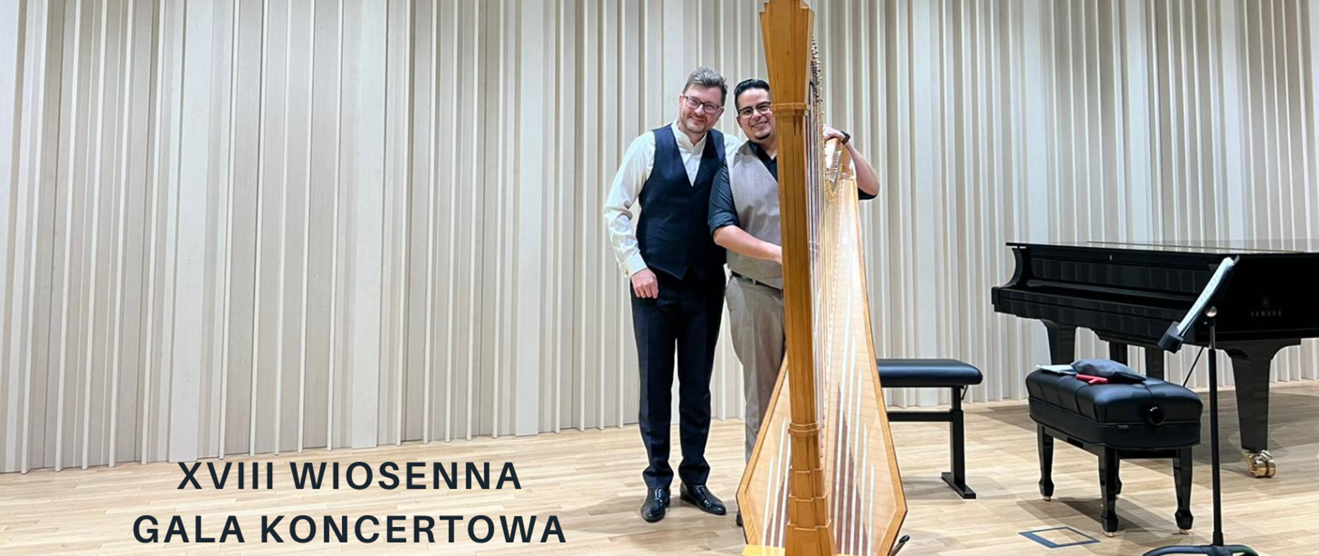 Na zdjęciu w centralnej części dwóch mężczyzna. Obaj noszą okulary. Jeden z nich w białej koszuli, czarnych spodniach i czarnej kamizelce. Drugi w czarnej koszuli, brązowych spodniach i brązowej kamizelce.Przed nim stoi harfa. Obok nich po prawej stronie czarny fortepian. Po lewej stronie mężczyzn czarny napis "XVIII Wiosenna Gala Koncertowa".