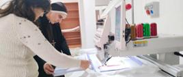 Dwie kobiety, w tym siostra zakonna, stoją przed maszyną do haftowania i czytają instrukcję obsługi