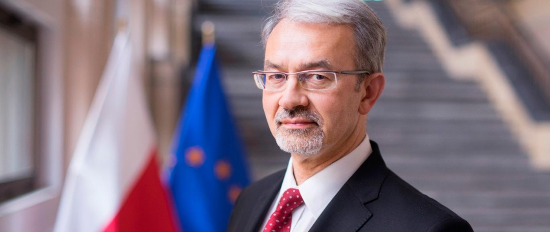 Minister Jerzy Kwieciński na tle flagi Polski i UE