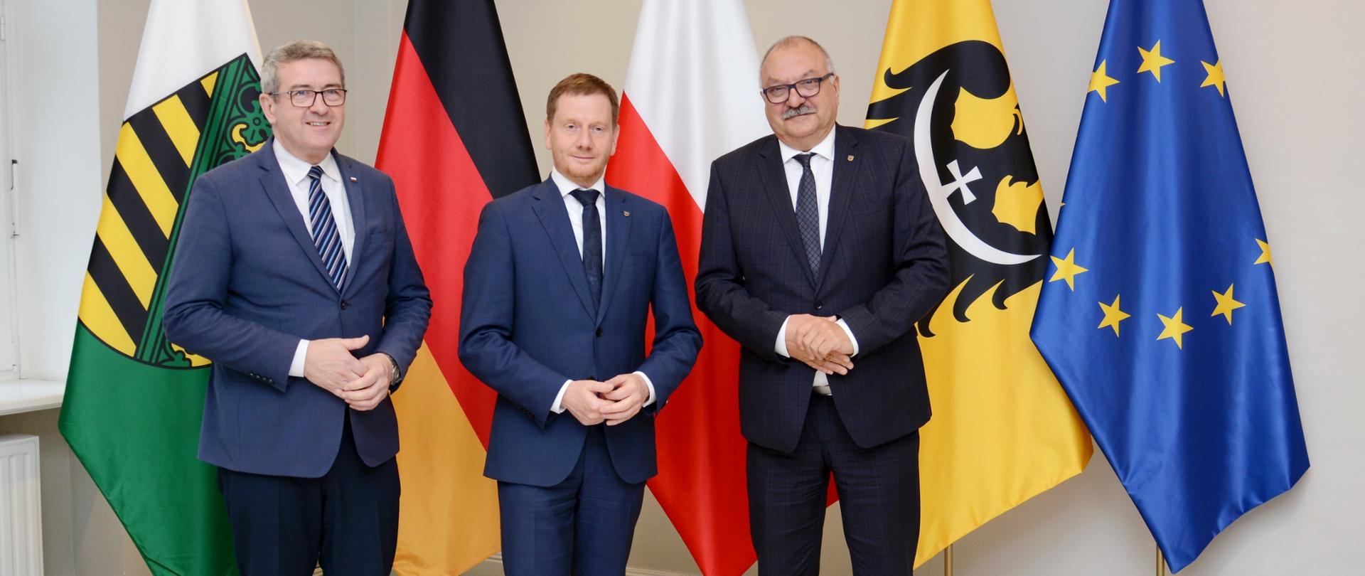 Na tle flag Polski, Dolnego Śląska, Niemiec, Saksonii i Unii Europejskiej stoją: minister Murdzek, marszałek Cezary Przybylski i premier Saksonii Michaele Kretschmer.