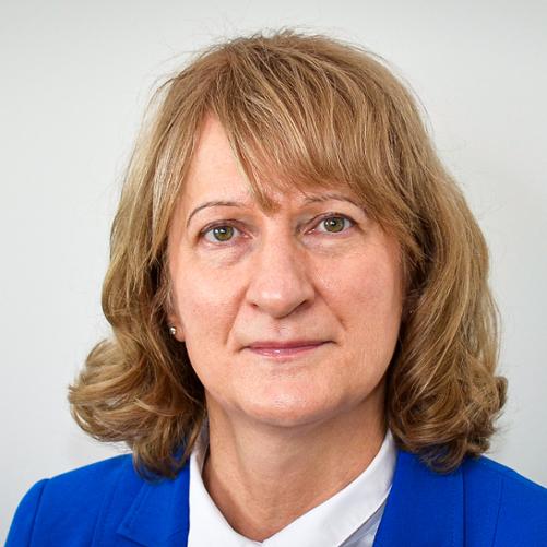 Kobieta w chabrowej marynarce i białej bluzce, z włosami do ramion. 