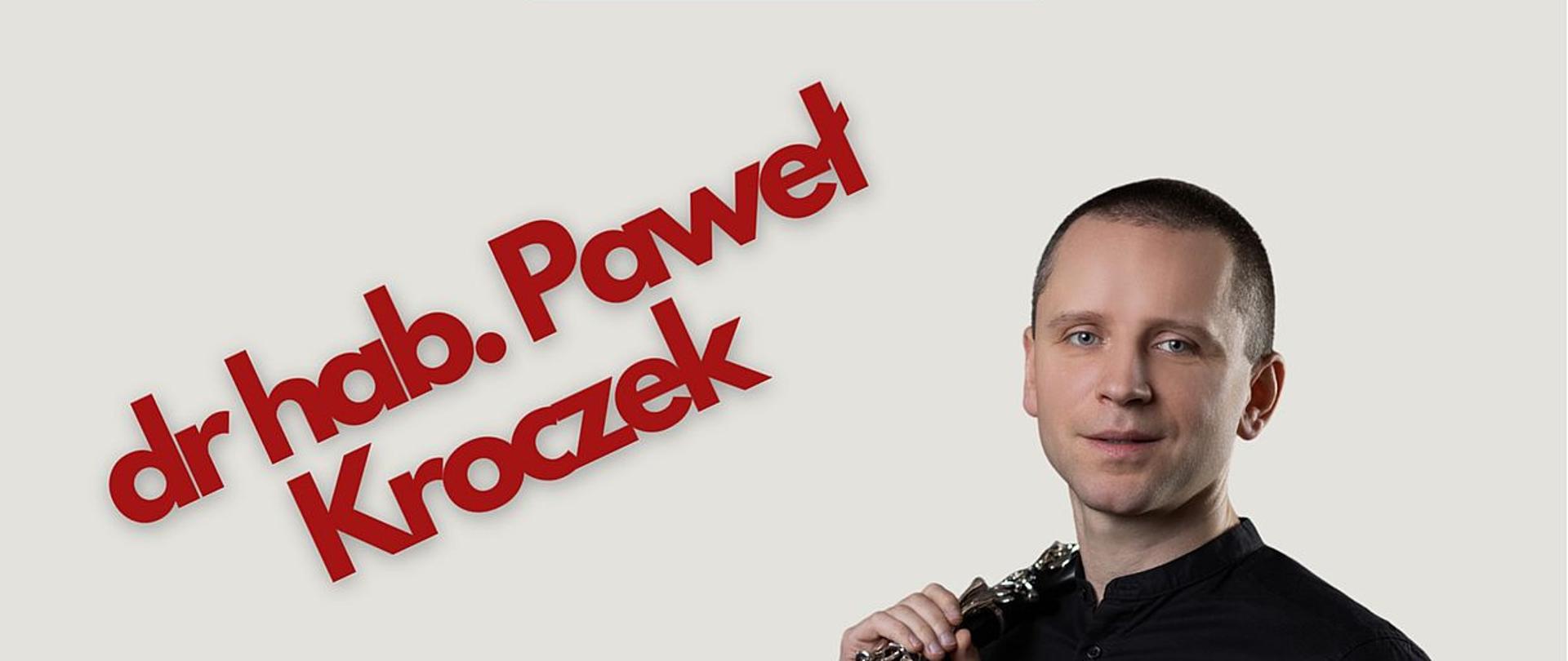 Zdjęcie przedstawia prowadzącego warsztaty doktora Pawła Kroczka trzymającego klarnet na szarym tle.