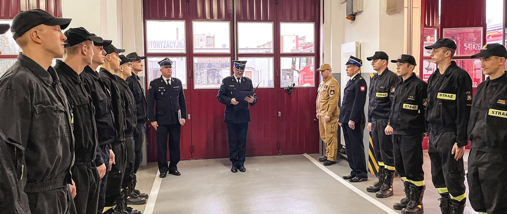 Komendant powiatowy występuje podczas uroczystego apelu. Po bokach stoją strażacy. Zdjęcie wykonane w garażu strażnicy.
