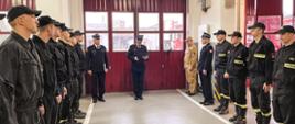 Komendant powiatowy występuje podczas uroczystego apelu. Po bokach stoją strażacy. Zdjęcie wykonane w garażu strażnicy.